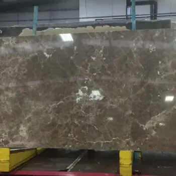 MA046 - Emperador: Large brown marble slab with white veining, displayed upright on yellow supports in an industrial warehouse.