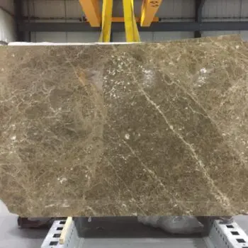 A large, rectangular slab of MA046 - Emperador polished brown marble with white veining is suspended by yellow straps in an industrial warehouse.