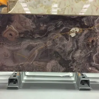 A large rectangular slab of ONX004 - Onice Viola, polished marble with dark brown and purple tones, lighter veins, and a yellowish streak, is displayed upright in an indoor warehouse.
